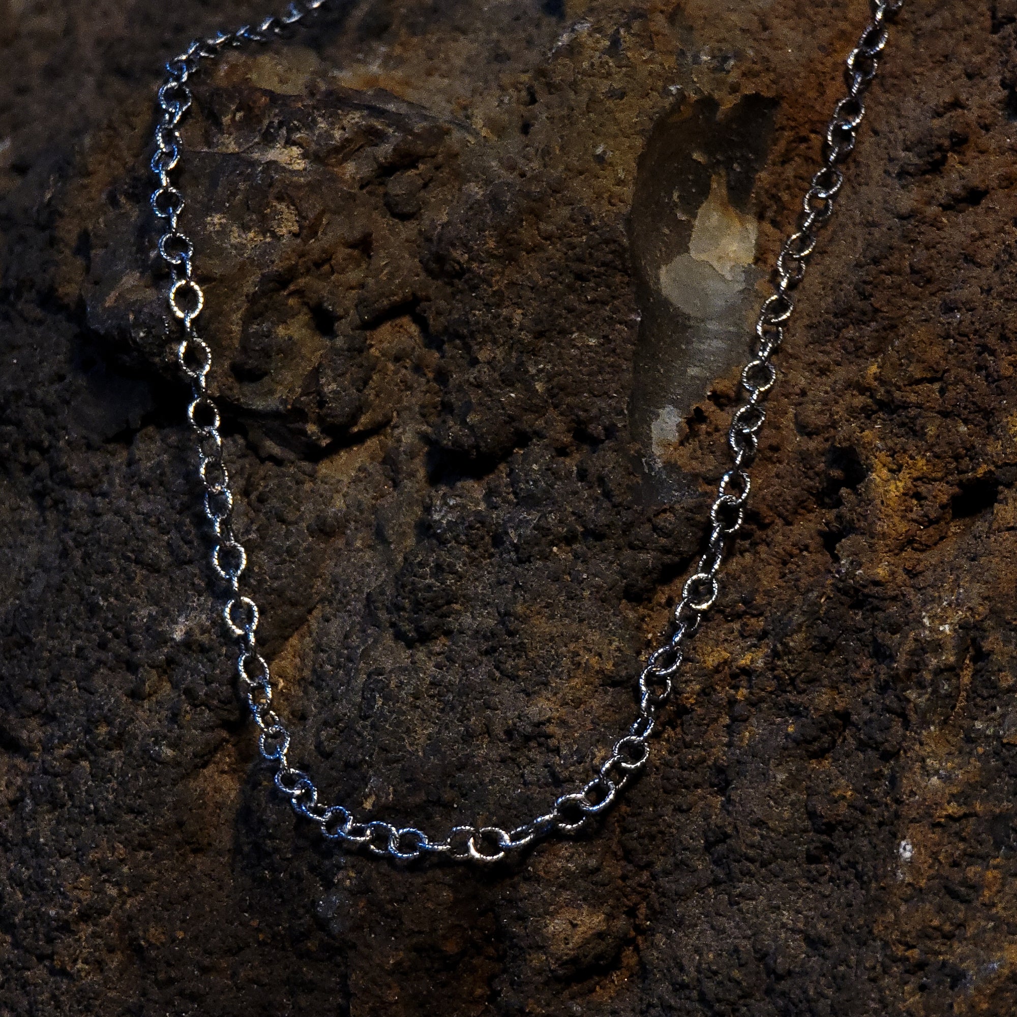 A sterling silver chain is draped over a rough rock. Each link on the chain looks as if two strands of silver have been twisted together and then twisted again to make a circle. 