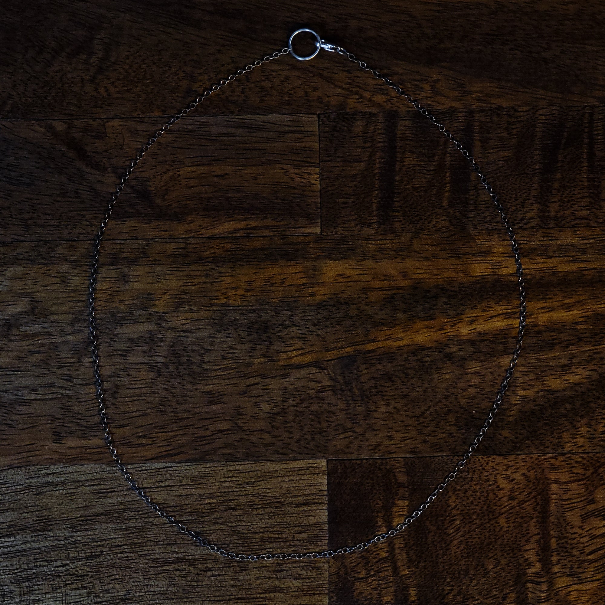 The chain is laid out on a wooden table. In this photo, you can see that the clasp attaches to a large jump ring closure. 