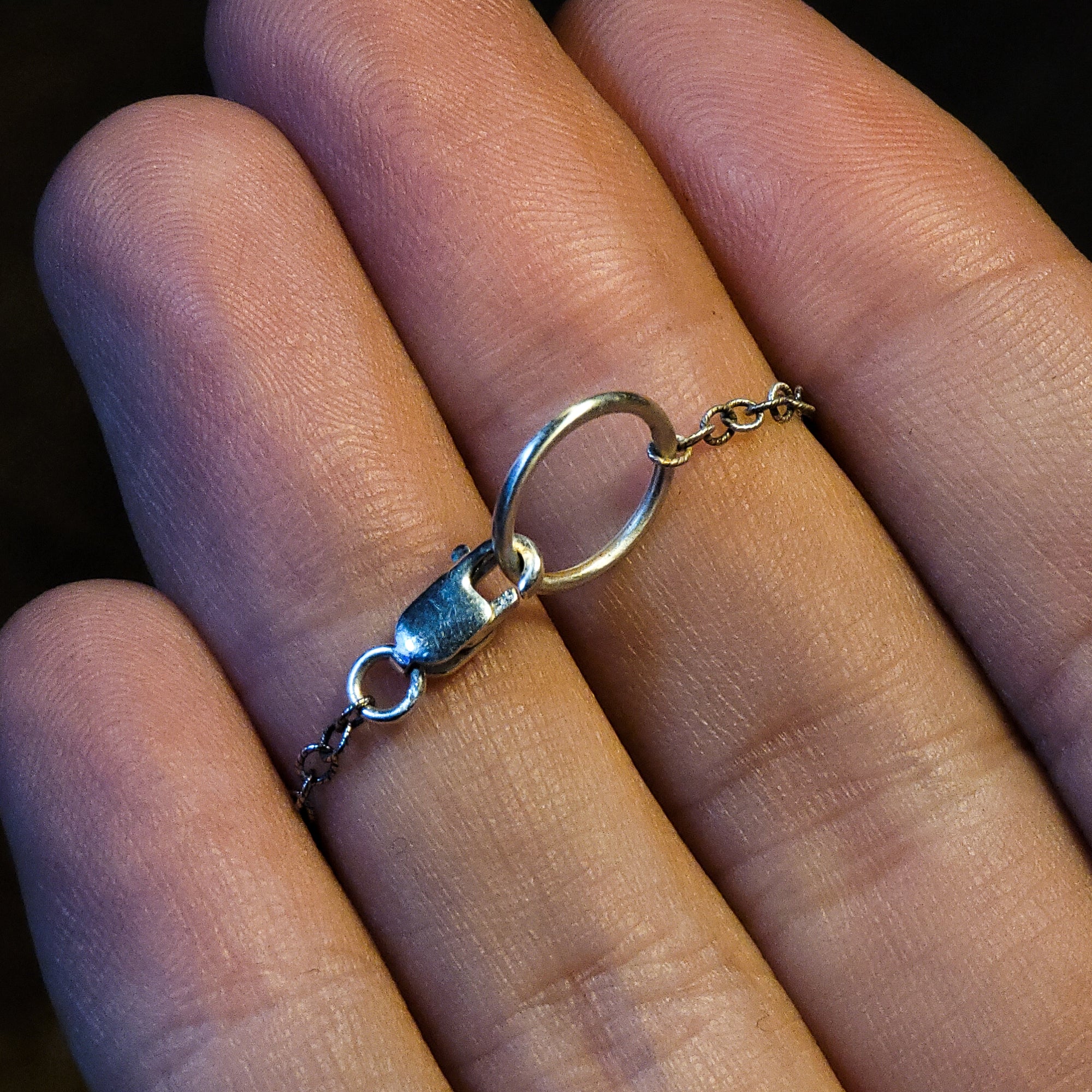 A closer look at the clasp of the chain. The clasp is being held by a human hand for size comparison. The jump ring is larger than average to help with putting the chain on. It has a traditional lobster clasp. 